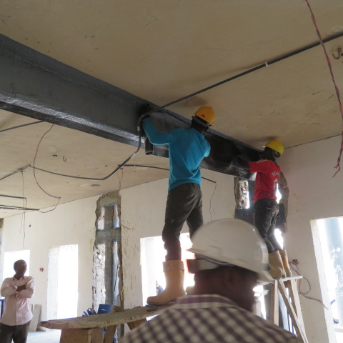 Operatives consolidating carbon fibre wrap along a strengthened beam