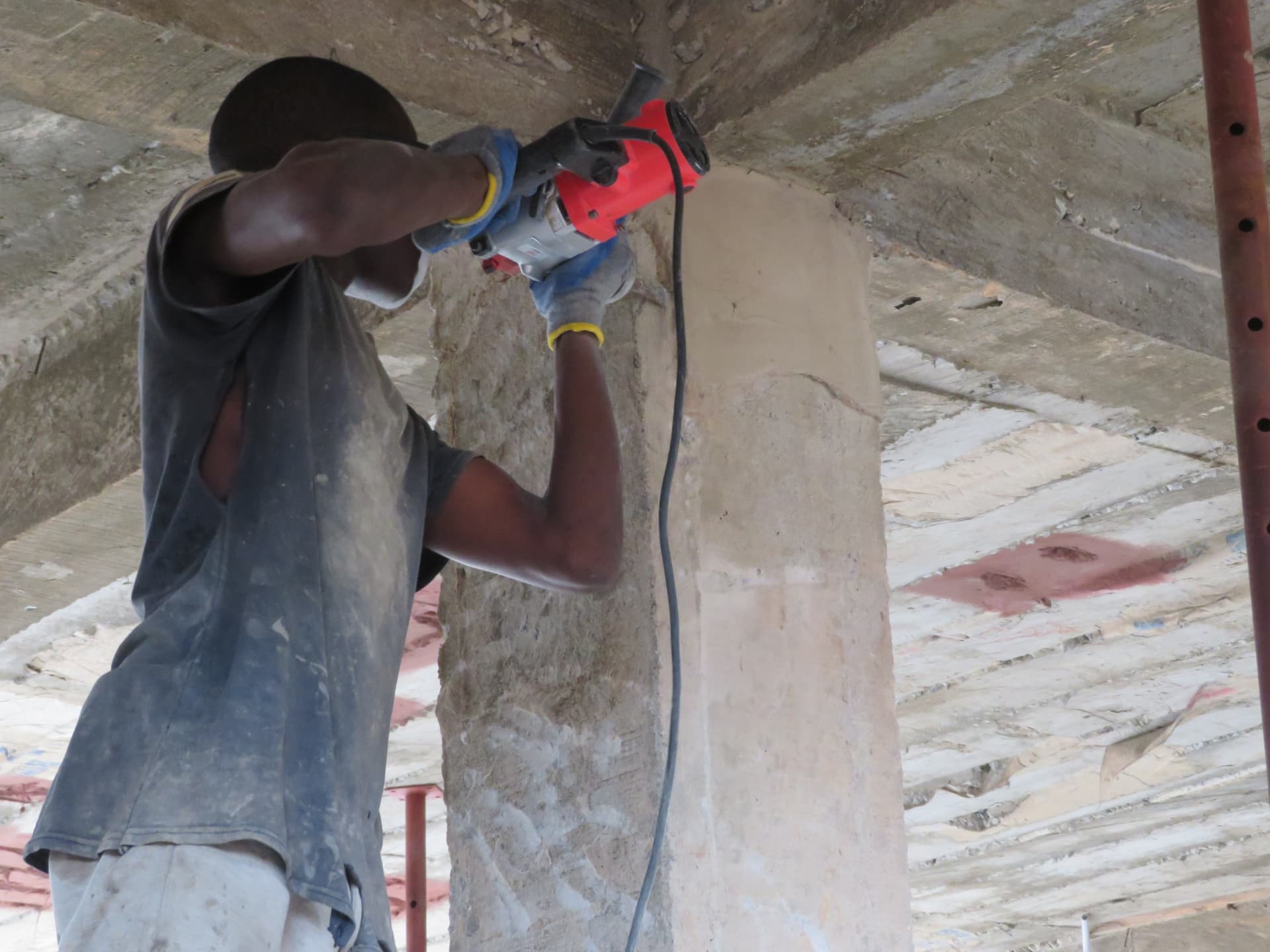 Worker cutting back defective concrete on a column with a reciprocating saw