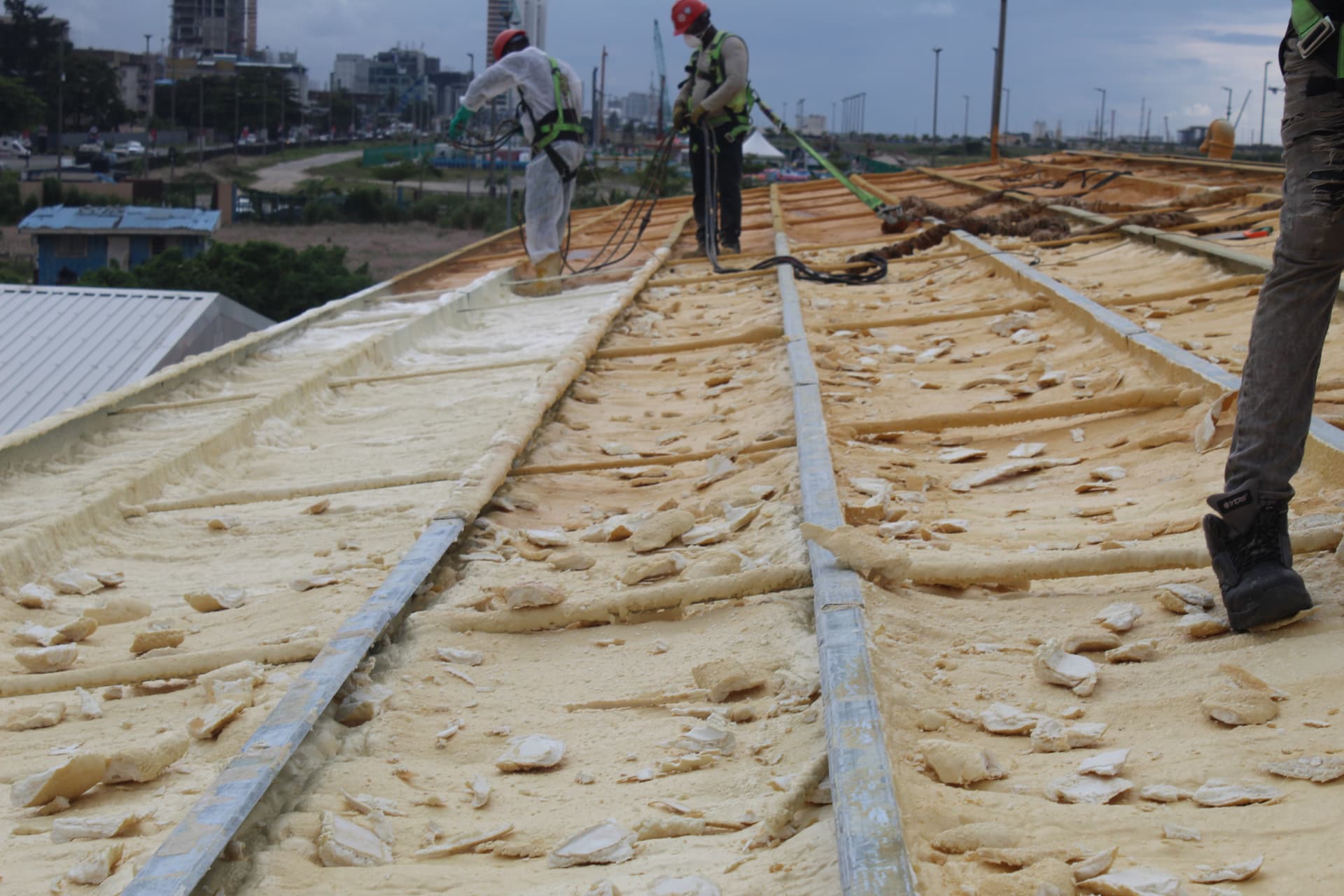 Spray foam crew working along the roof ridge with the Lagos skyline behind