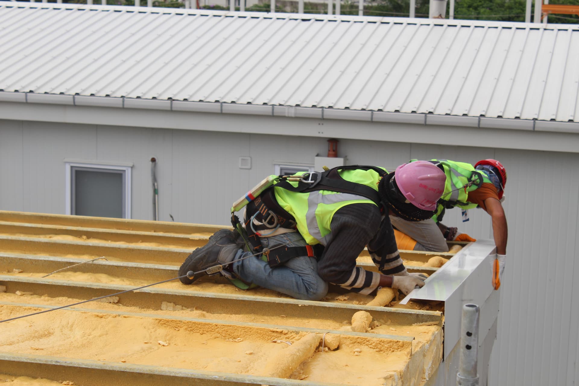 Operatives in harnesses fixing roof edge trim over the foamed roof bays