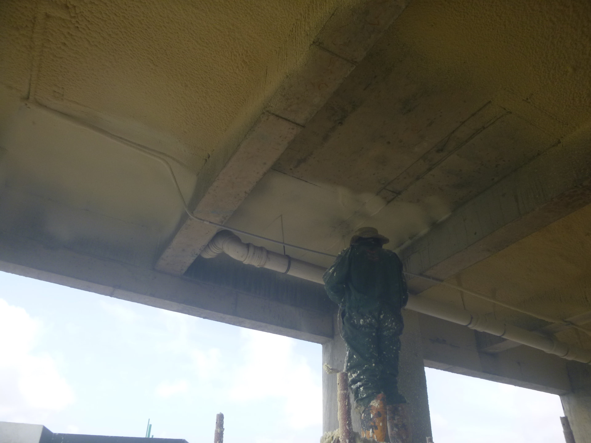 Spray applicator working along the slab edge beside service pipework