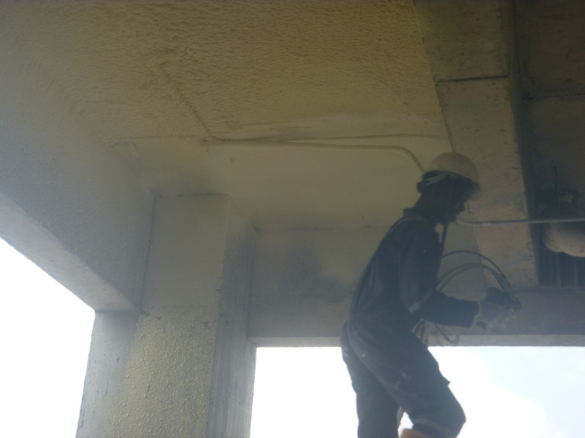 Applicator spraying foam around a beam and column junction