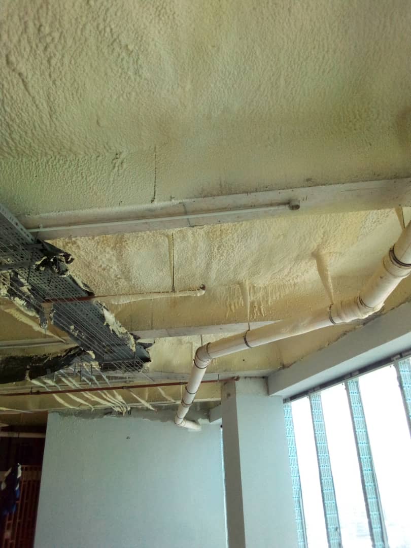 Close view of the applied foam layer around pipework at the ceiling